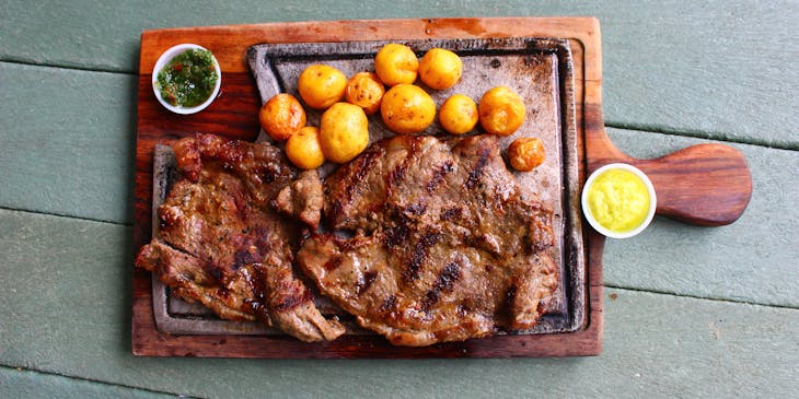 Plato de parrillada con dos vasos de aderezo sobre una superficie de madera en un restaurante colombiano.