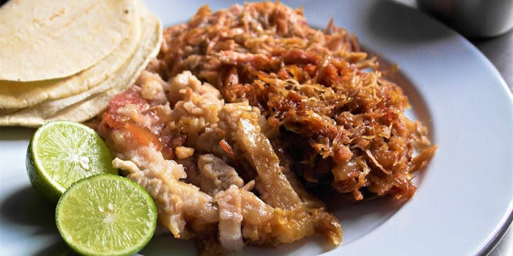 Un plato servido con carnitas tortillas y limón acompañadas de 3 salseros con cebolla cilantro y salsa verde en un restaurante de carnitas.