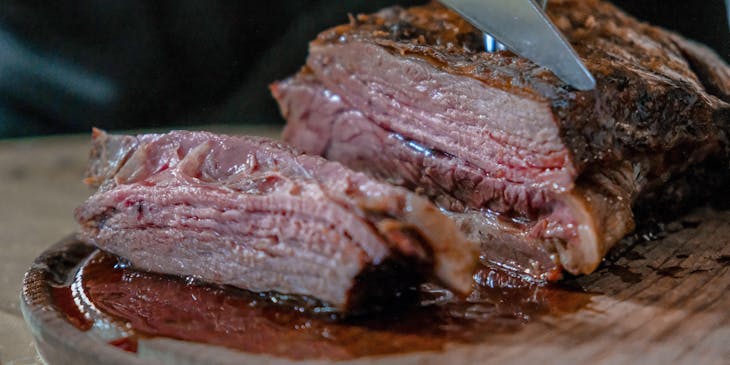 Un pernil asado siendo cortado con un cuchillo muy filoso sobre una tabla de madera por un mesero en un restaurante de pernil asado.