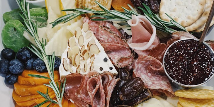 Una tabla llena de quesos, carnes frías, frutas secas y galletas para acompañar en un restaurante de picadas.