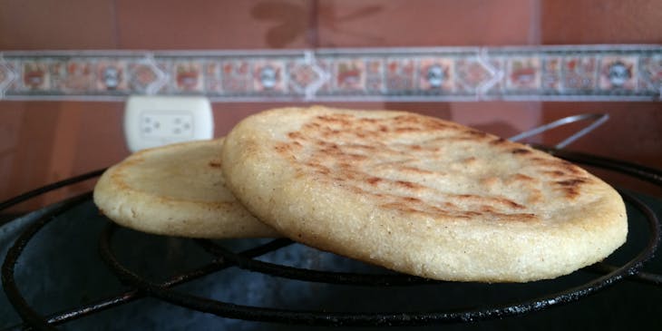 Dos arepas sobre una parrilla con una pared y un contacto eléctrico al fondo en un restaurante venezolano.