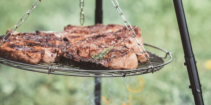 Tres cortes de carne asándose en una parrilla al aire libre fuera de un restaurante de parrillas.