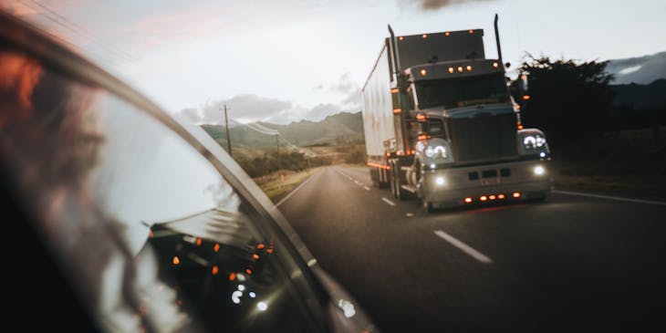 Vista de un tráiler de un servicio de fletes en la carretera con los faros encendidos.