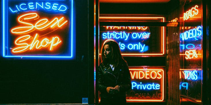 Una mujer usando una chamarra negra frente a una sex shop.