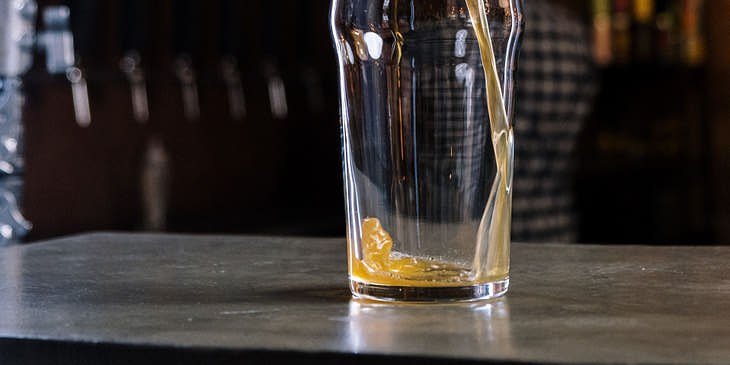 Una mano sirviendo sidra en un vaso en la barra de una sidrería.