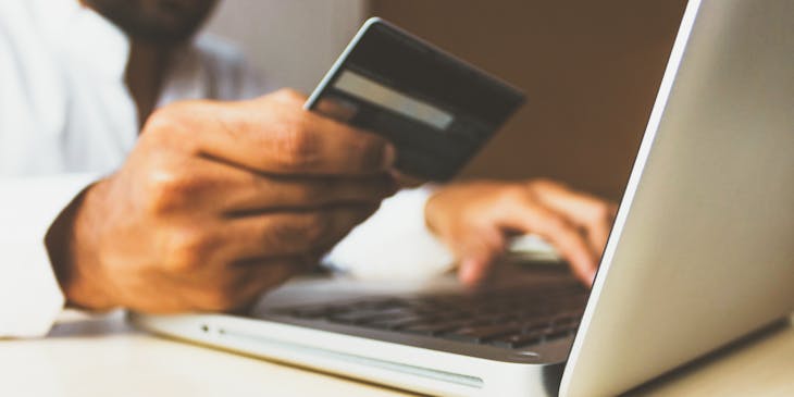 Hombre haciendo compras en una smart shop a través de su laptop con una tarjeta de crédito en la mano derecha.