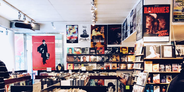 El interior de una tienda de música llena de discos de vinilo, pósters e instrumentos musicales.