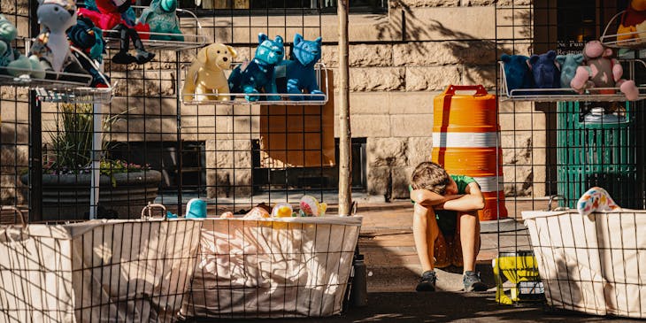 Un niño sentado en una venta de garage con juguetes acomodados en estantes.