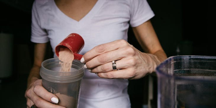 Mulher pegando um scoop de whey protein.