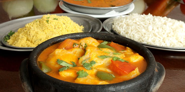 Prato de moqueca, arroz e farofa na frente de alguns temperos em um restaurante capixaba