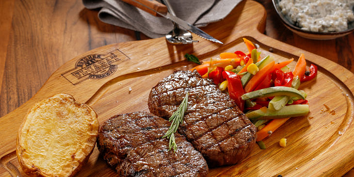 Tábua com churrasco, legumes e pão em um restaurante gaúcho