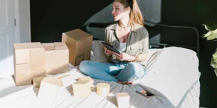 An online store business owner working on a tablet with boxes of items ready to be shipped.