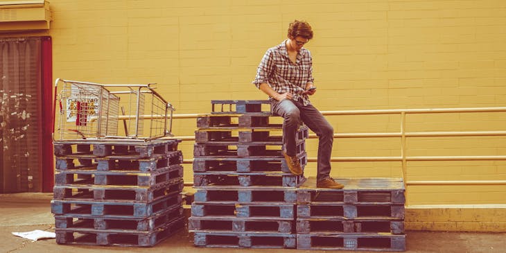 A man sitting on top of a stack of pallets.