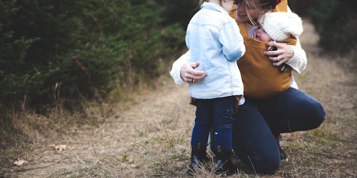 Woman carrying her baby talks to her older child.