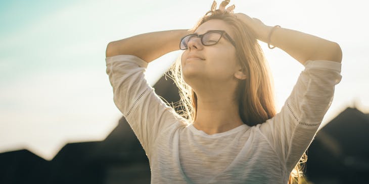 A woman with closed eyes looking peaceful while doing a stretch on a sunny day.