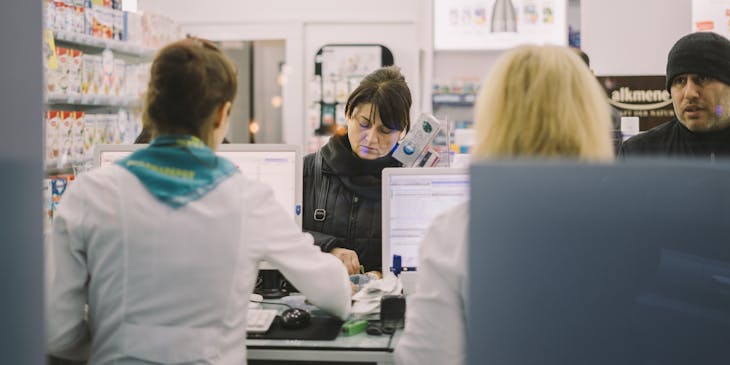 Una mujer comprando medicamentos a un empleado de una farmacia.