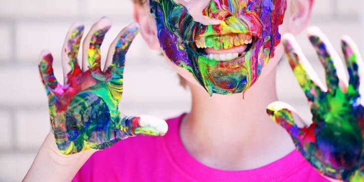 A playful child with paint on their face and hands.