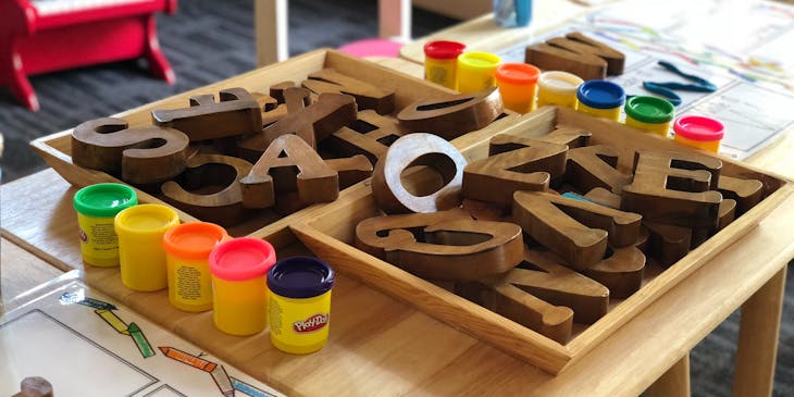 Children's desk set up with wooden alphabet pieces and colorful play doh sets at a preschool business.