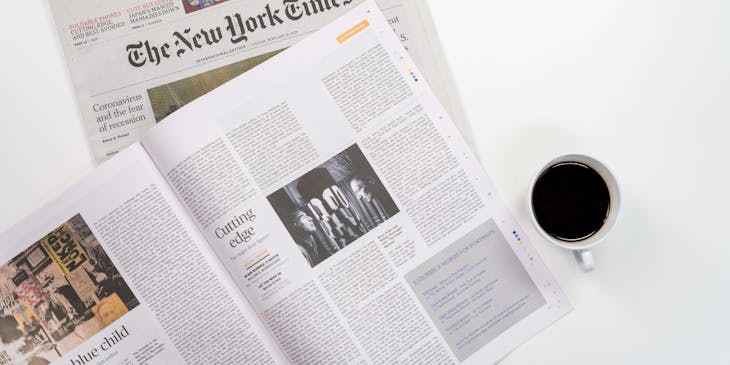 Un periódico y una revista de medios impresos junto a una taza de café.