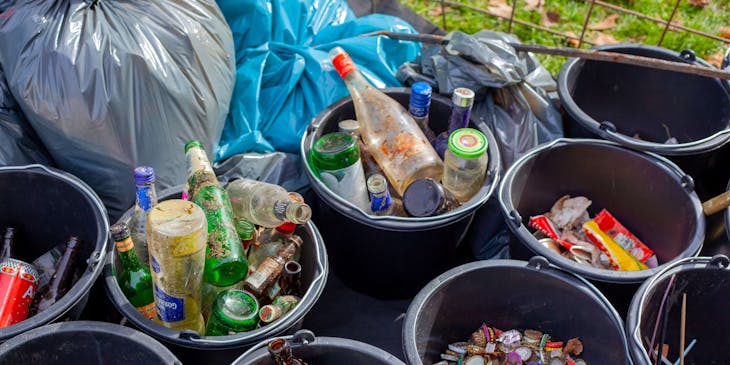 Garrafas de vidro e canudos separados em baldes de plástico em um centro de reciclagem.