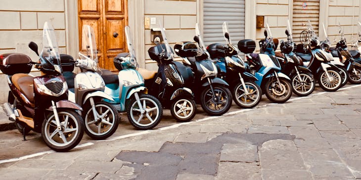 Fileira de scooters azuis, brancas e pretas do lado de fora de uma empresa de scooters.