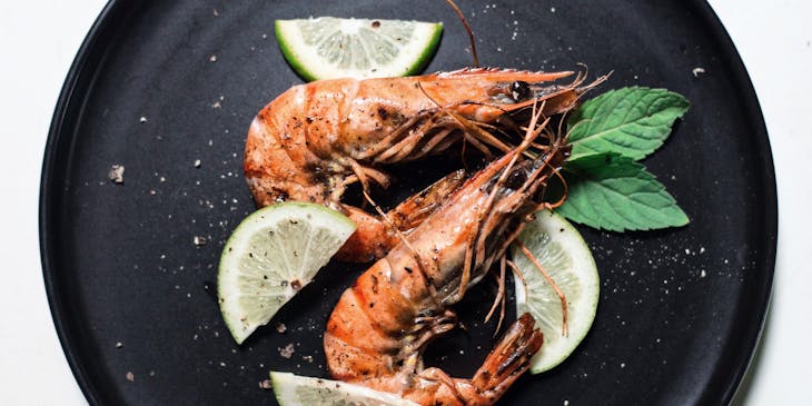 Two shrimp garnished with sliced lime and two basil leaves.