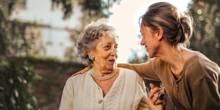 Smiling woman bent over while speaking to an elderly woman.