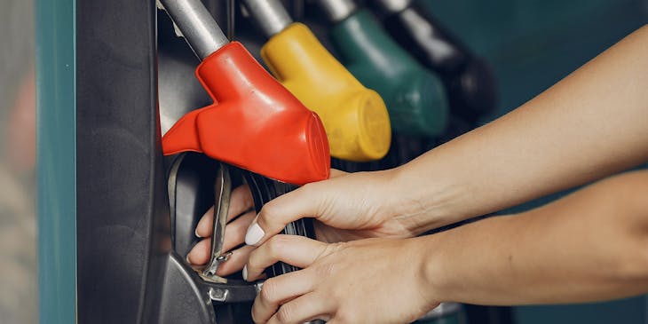 Woman's hands picking up a red gas pistol pump at a service station.