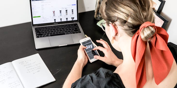 Una donna che guarda il cellulare mentre si trova davanti al pc per organizzare un piano di social media marketing.