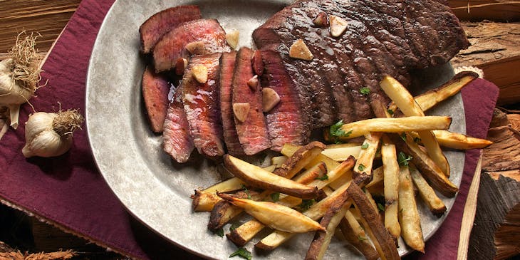 Un filete con papas a la francesa sobre un plato blanco en un restaurante de carnes.