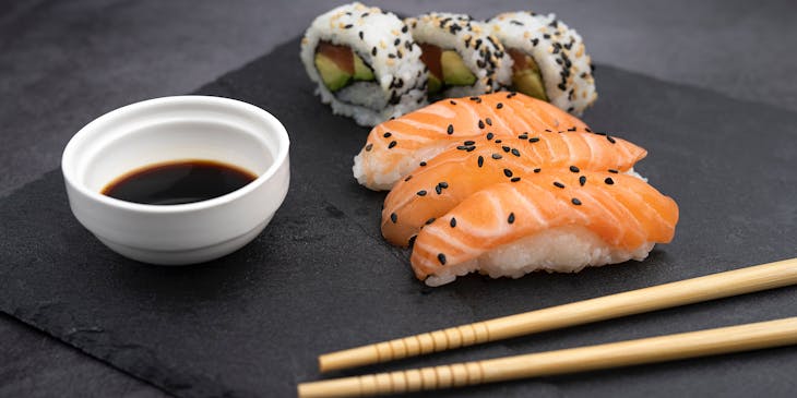 Nigiri de salmón y rollos california con salsa de soya en un plato negro y palillos chinos en un sushi bar.