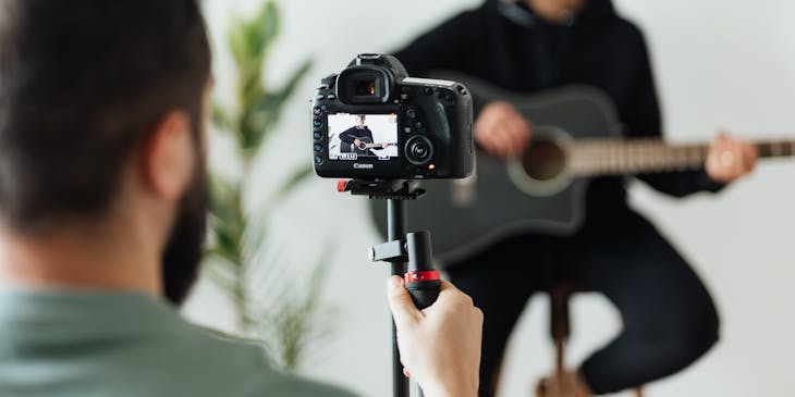 Un homme en train de filmer un autre homme jouant de la guitare.