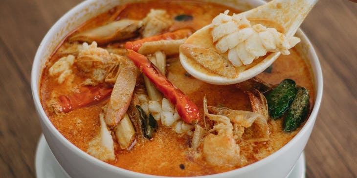 Sopa tailandesa de coco en un bowl de cerámica blanca sobre una mesa de madera