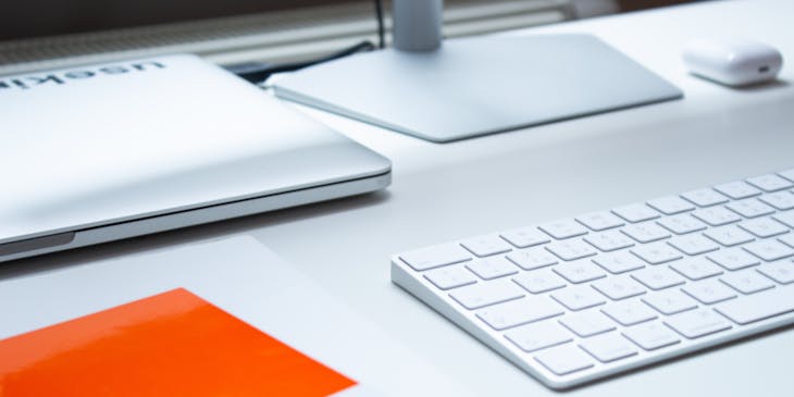 Livro, laptop e computador, teclado e mouse em cima de uma mesa de escritório branca