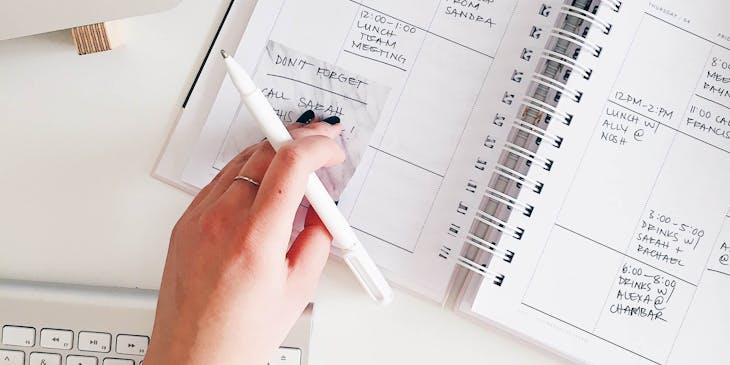 A virtual assistant holding a pen and placing a sticky note on a planner.