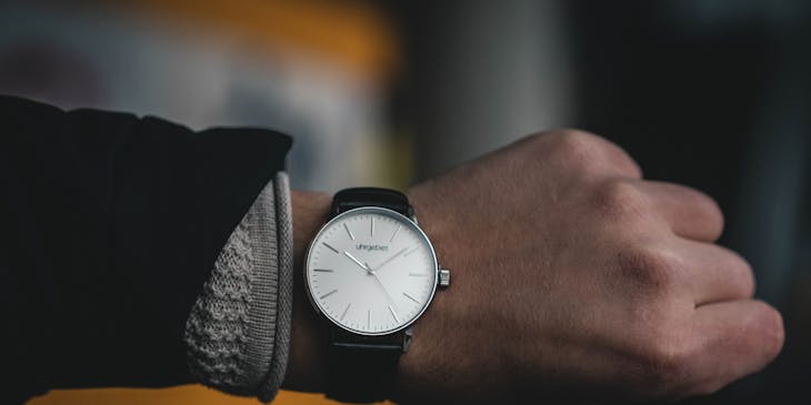 Montre avec un bracelet en cuir et un cadran blanc au poignet d'une personne.