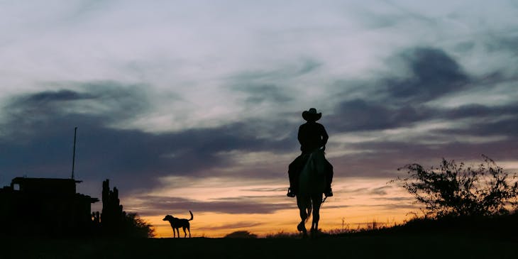 Silueta de un vaquero a caballo contra la puesta de sol en un negocio estilo western.