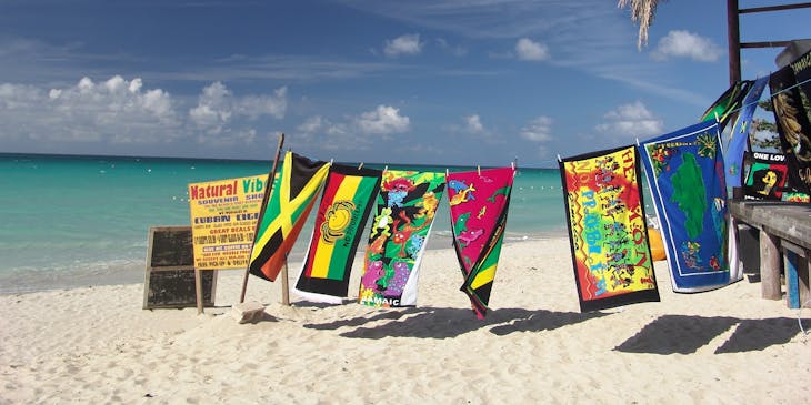 Una playa con un tendedero con toallas con temáticas jamaiquinas a lado de una palapa de un negocio con nombre jamaiquino.