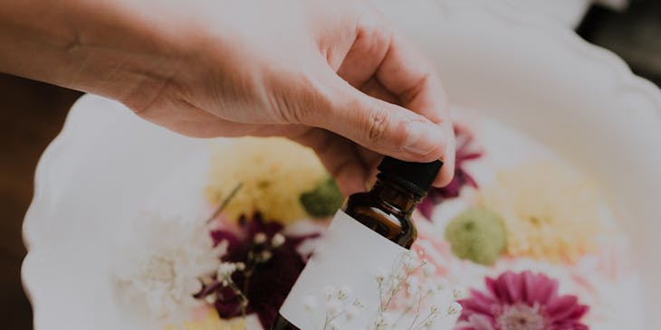 Une personne tenant une bouteille d'huile essentielle sur des fleurs.